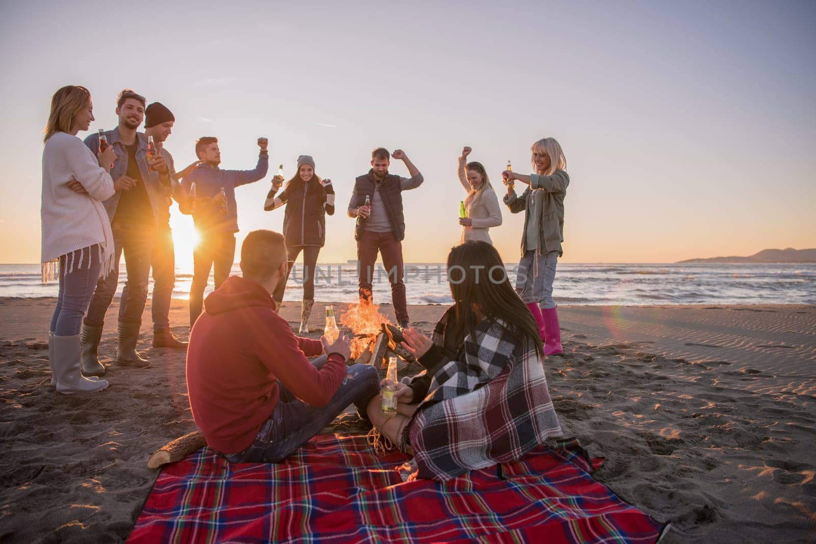 Young Couple enjoying with friends Around Campfire on The Beach At sunset drinking beer