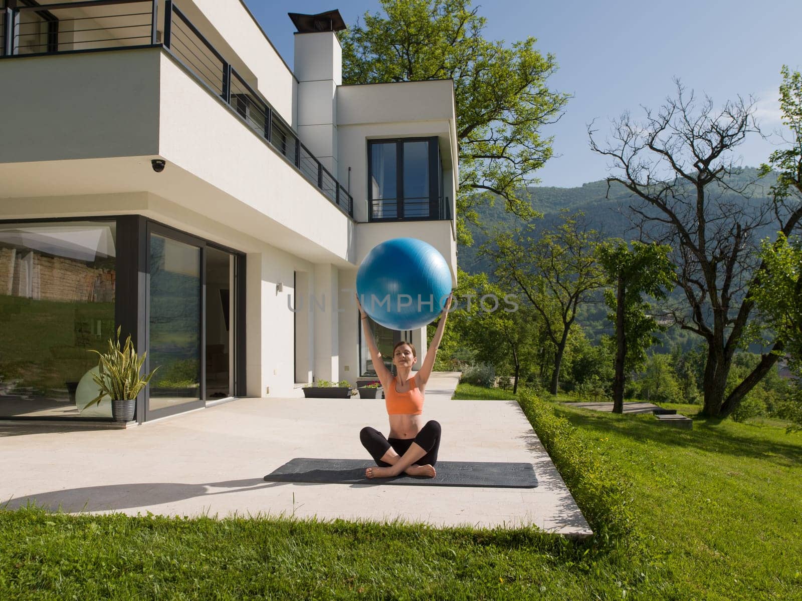 young beautiful woman doing exercise with pilates ball in front of her luxury home villa