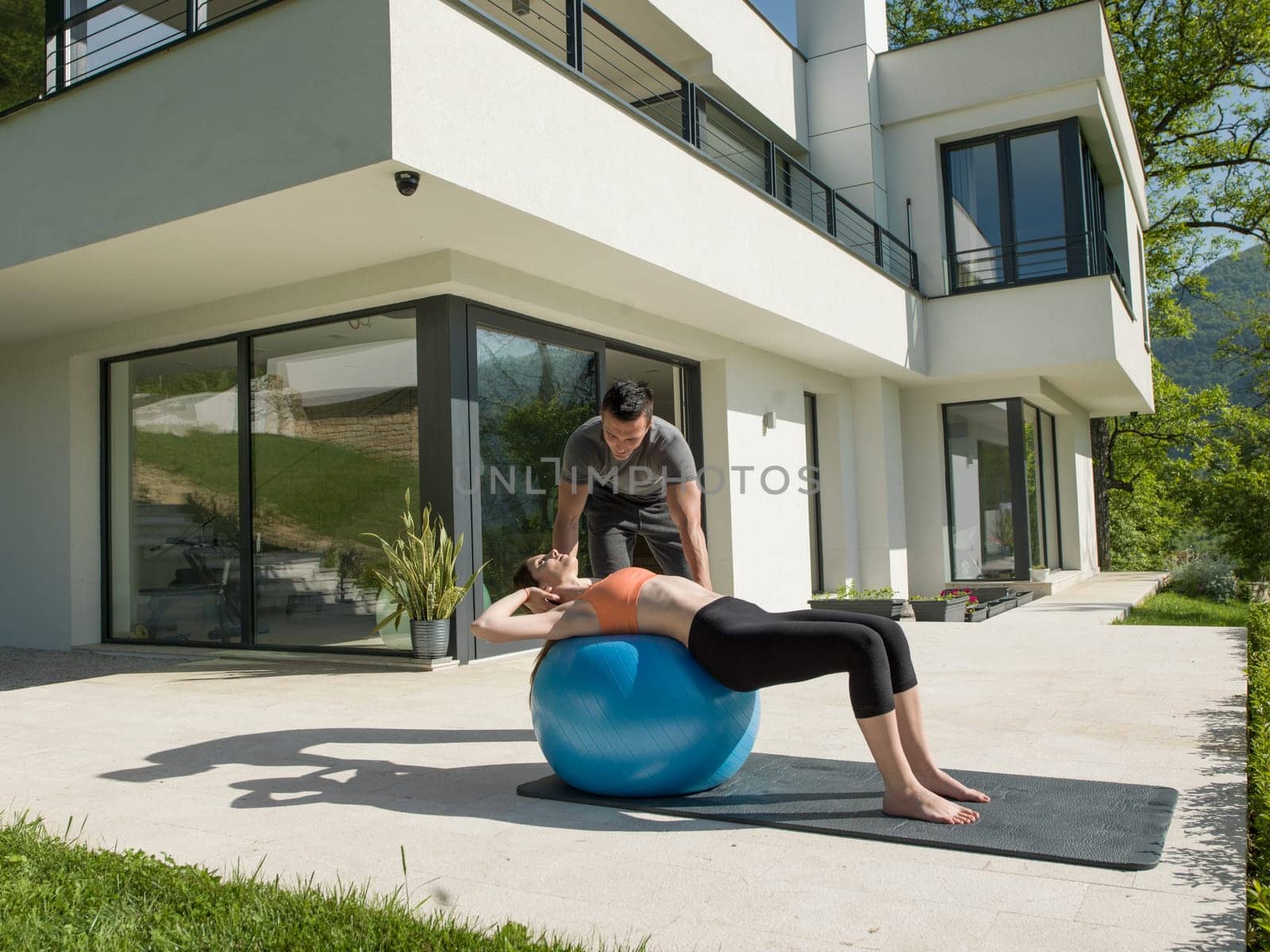 young beautiful woman and personal trainer doing exercise with pilates ball in front of her luxury home