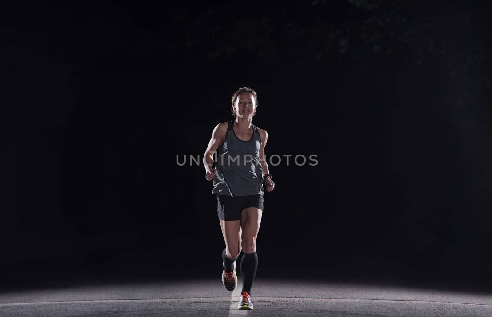 fit muscular female runner training for marathon running at night on beautiful road in nature.