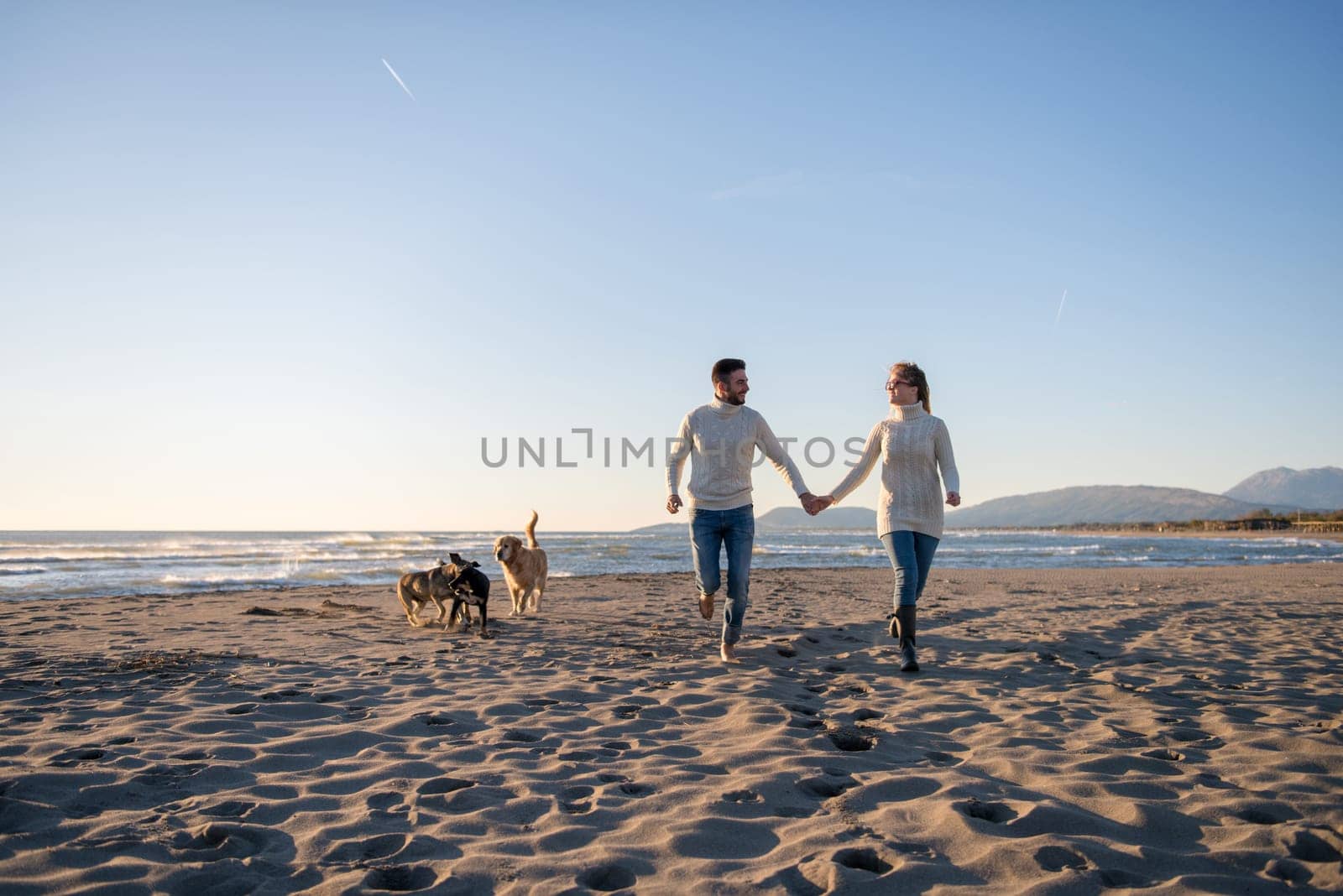 Couple Running On The Beach Holding Their Hands with dog On autmun day