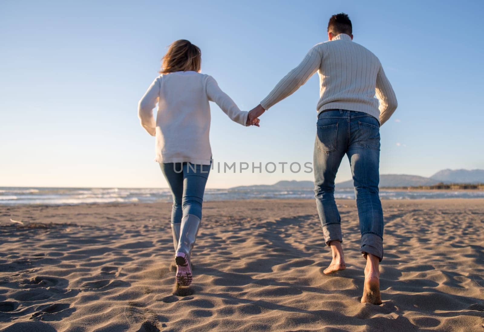 Young couple having fun walking and hugging on beach during autumn sunny day