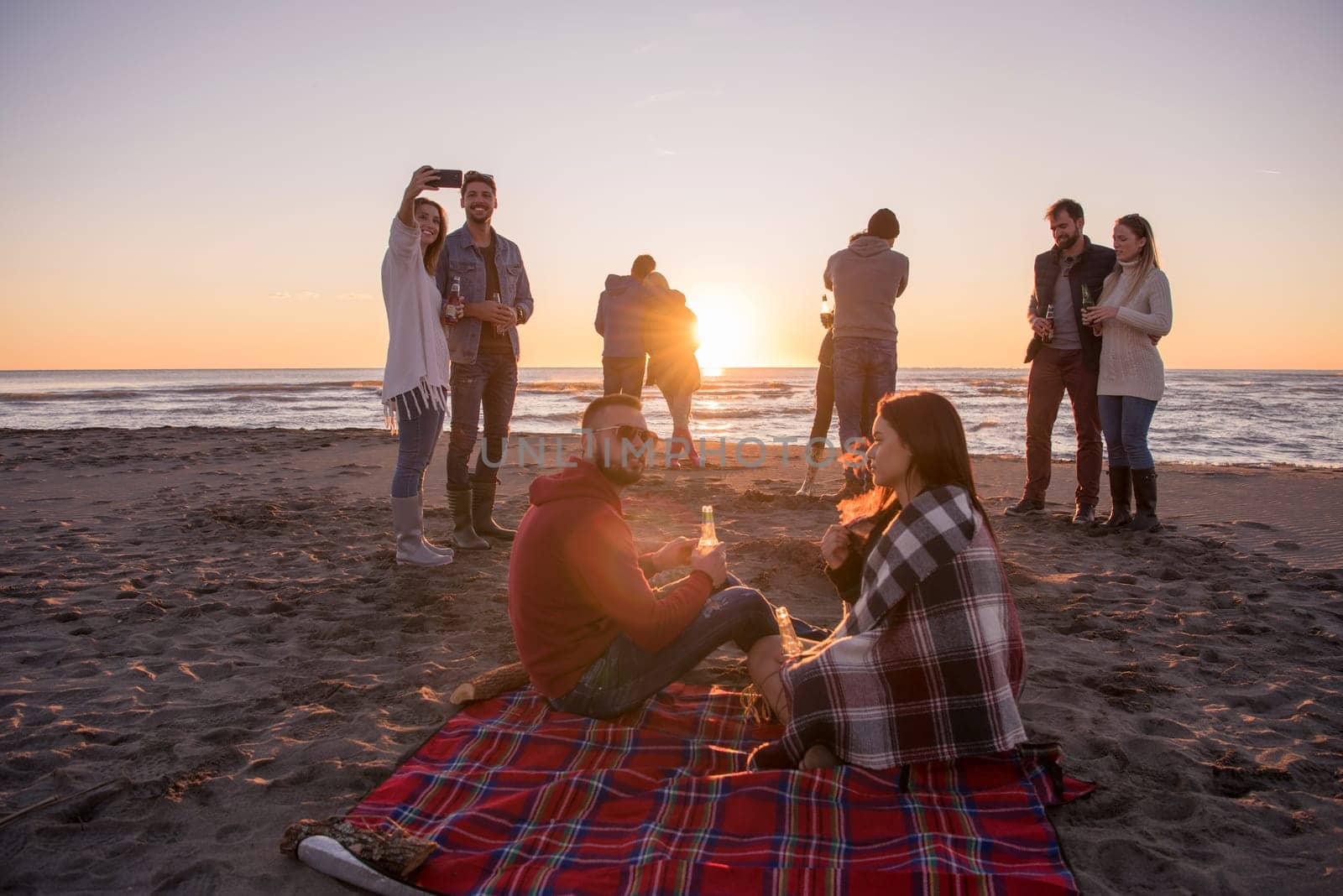 Young Couple enjoying with friends Around Campfire on The Beach At sunset drinking beer
