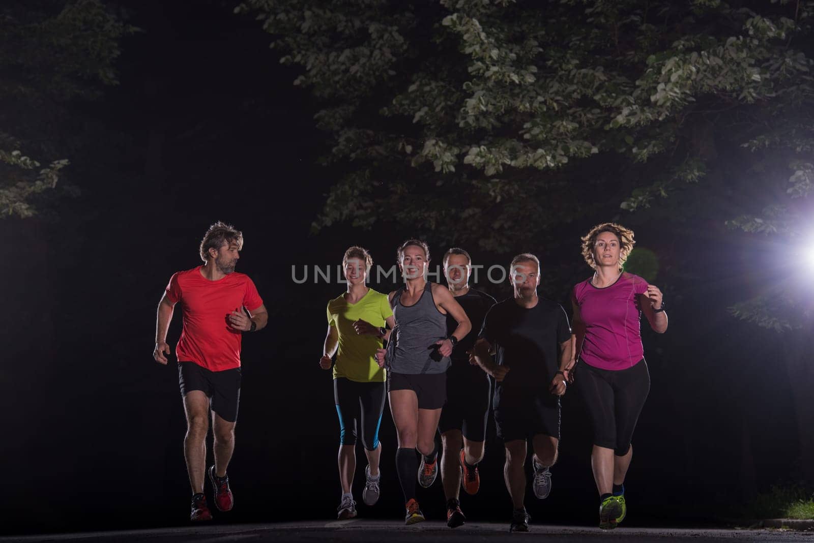 group of healthy people jogging in city park, runners team at night training