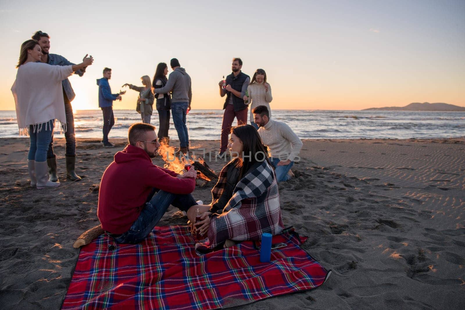 Young Couple enjoying with friends Around Campfire on The Beach At sunset drinking beer