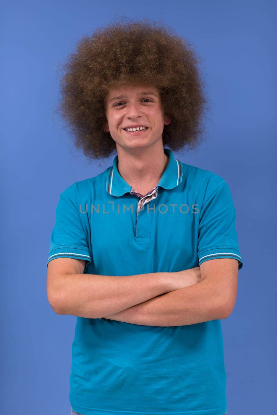portrait of a young man with a funky hairstyle with arms crossed on blue background