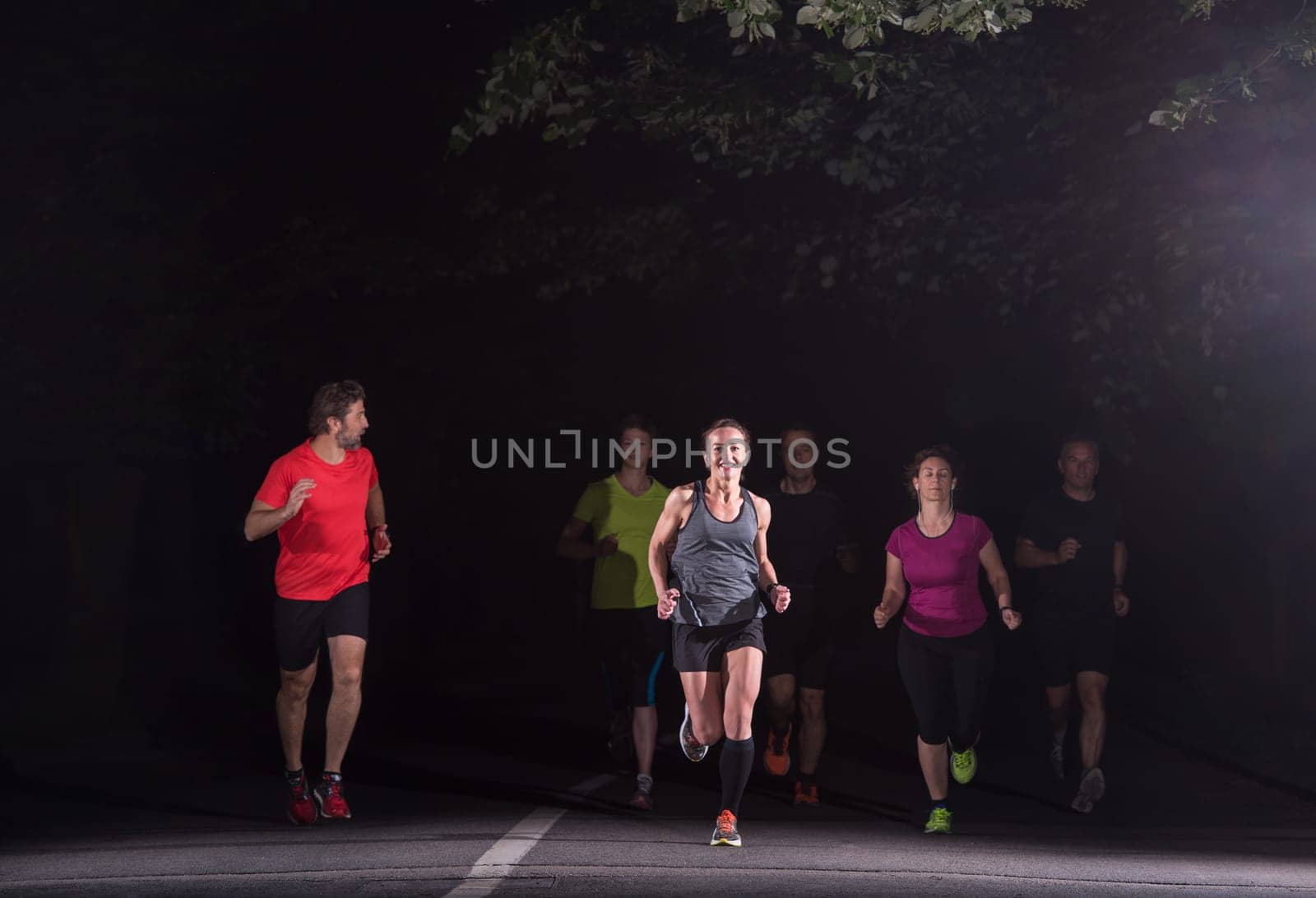 group of healthy people jogging in city park, runners team at night training