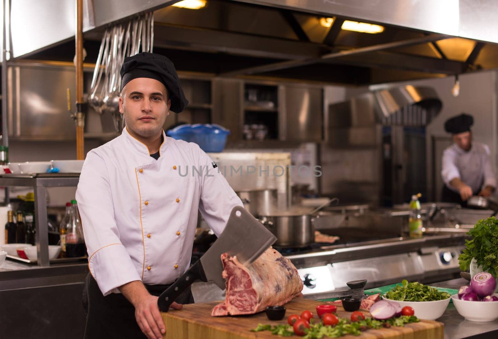 chef using ax while cutting big piece of beef  on wooden board in restaurant kitchen