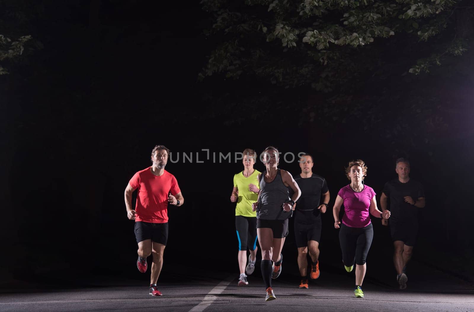 group of healthy people jogging in city park, runners team at night training