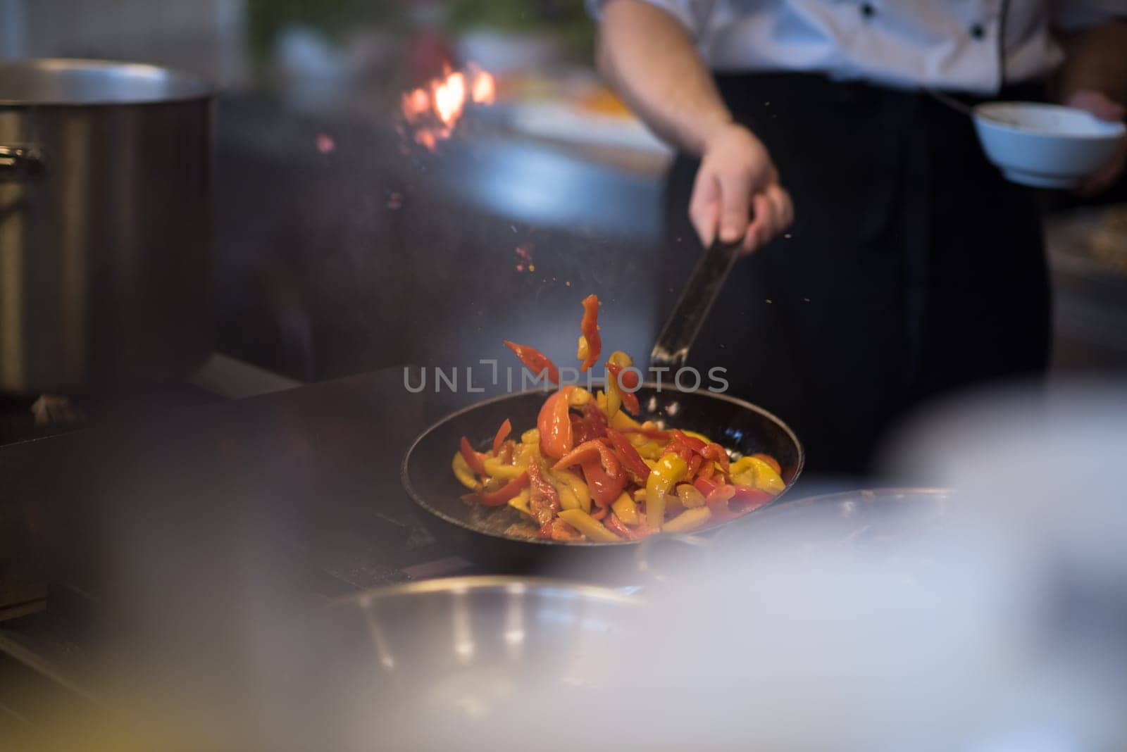 Young male chef flipping vegetables in wok at commercial kitchen