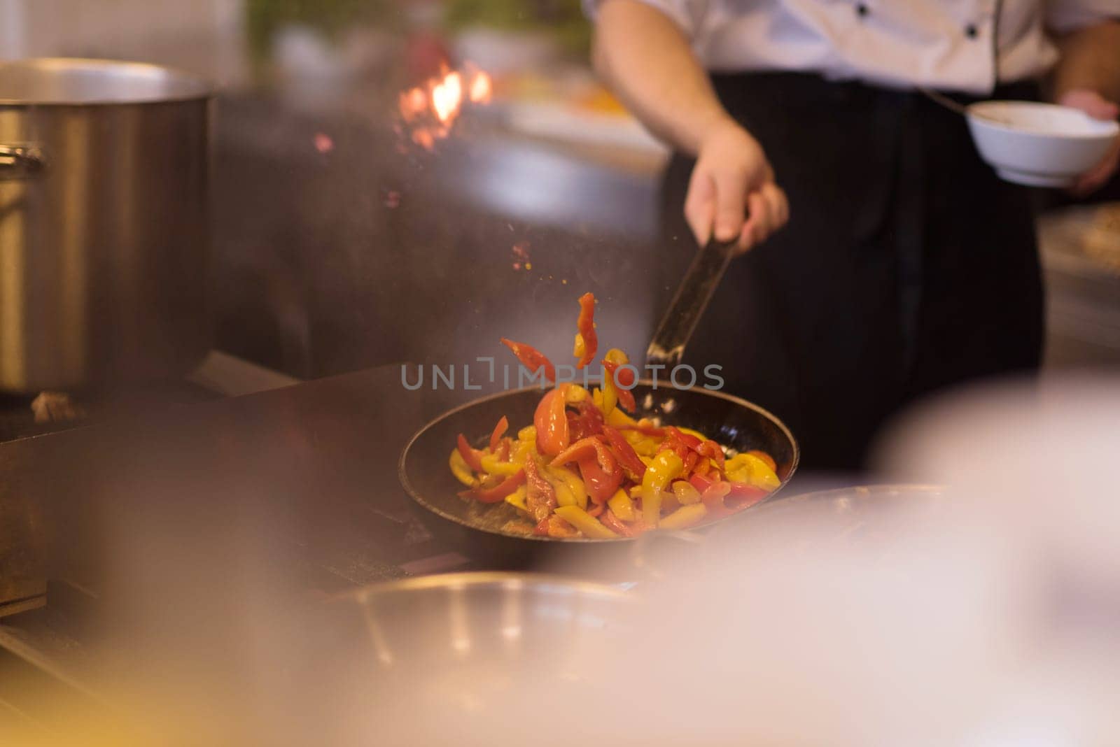 Young male chef flipping vegetables in wok at commercial kitchen
