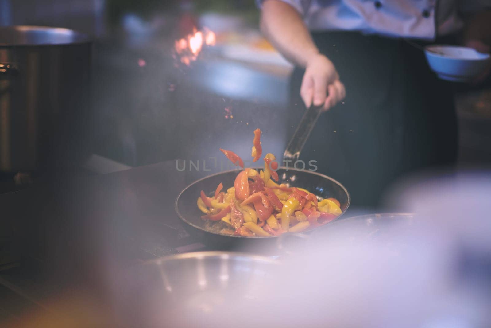 Young male chef flipping vegetables in wok at commercial kitchen