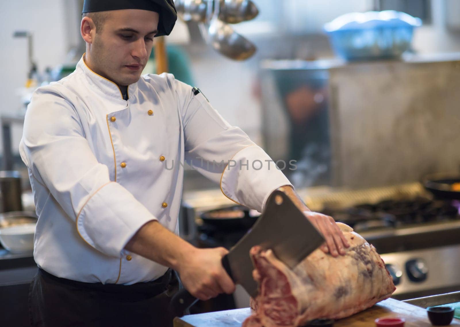 chef using ax while cutting big piece of beef  on wooden board in restaurant kitchen