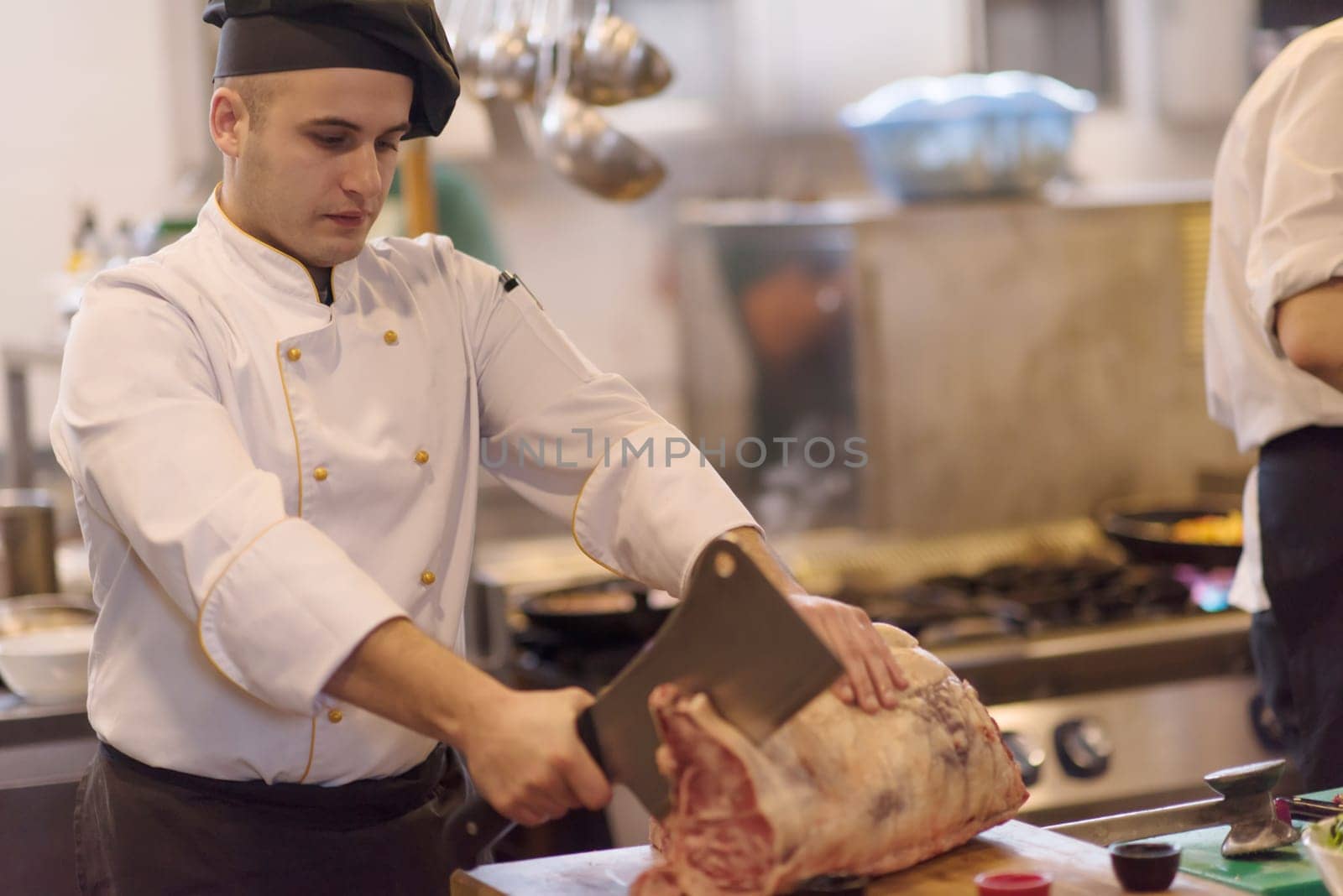 chef using ax while cutting big piece of beef  on wooden board in restaurant kitchen