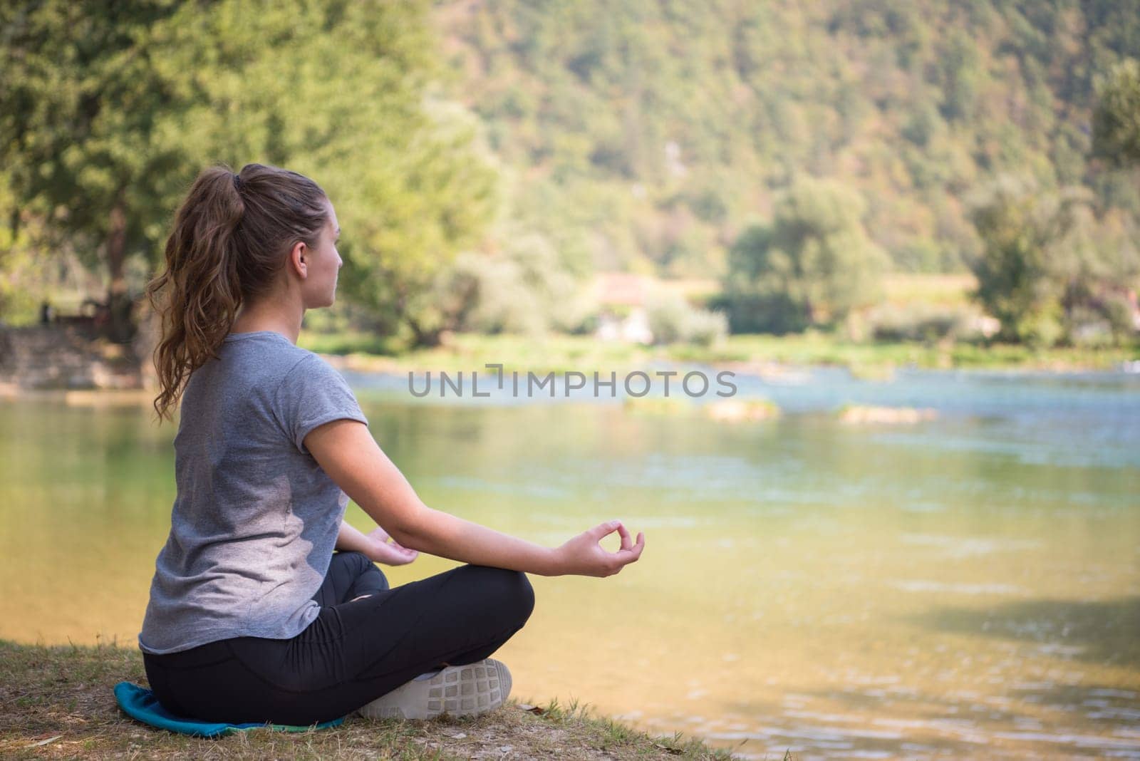 healthy woman relaxing while meditating and doing yoga exercise in the beautiful nature on the bank of the river