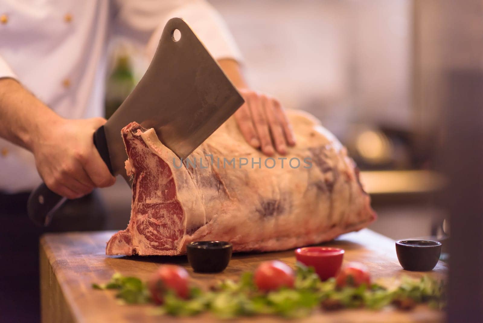 chef using ax while cutting big piece of beef  on wooden board in restaurant kitchen