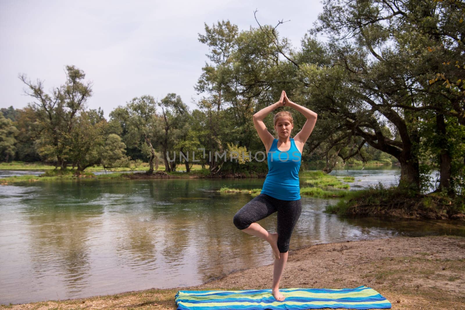 healthy woman relaxing while meditating and doing yoga exercise in the beautiful nature on the bank of the river
