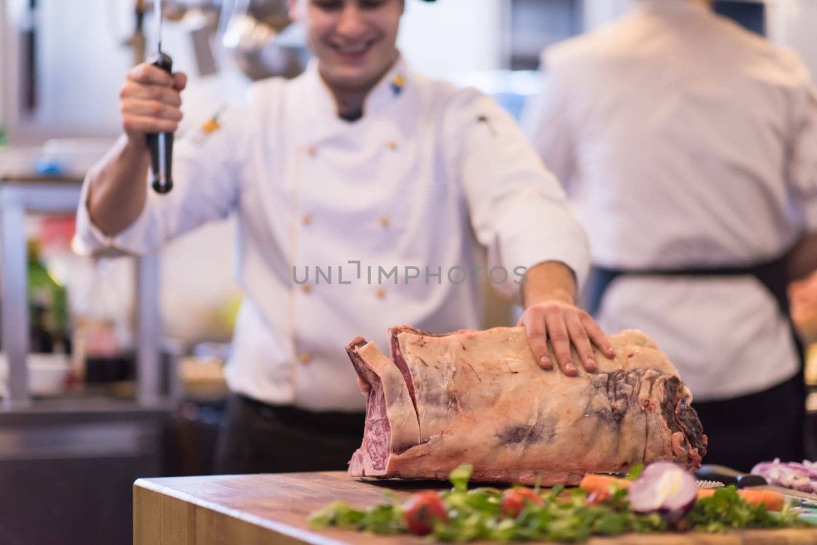 chef using ax while cutting big piece of beef  on wooden board in restaurant kitchen