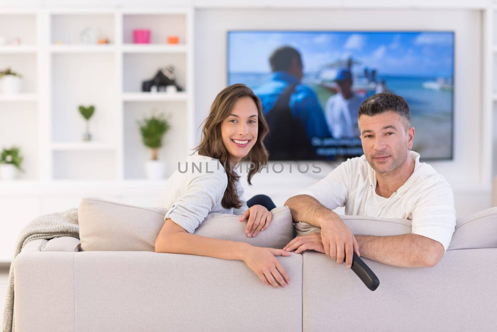 Young couple on the sofa watching television together in their luxury home
