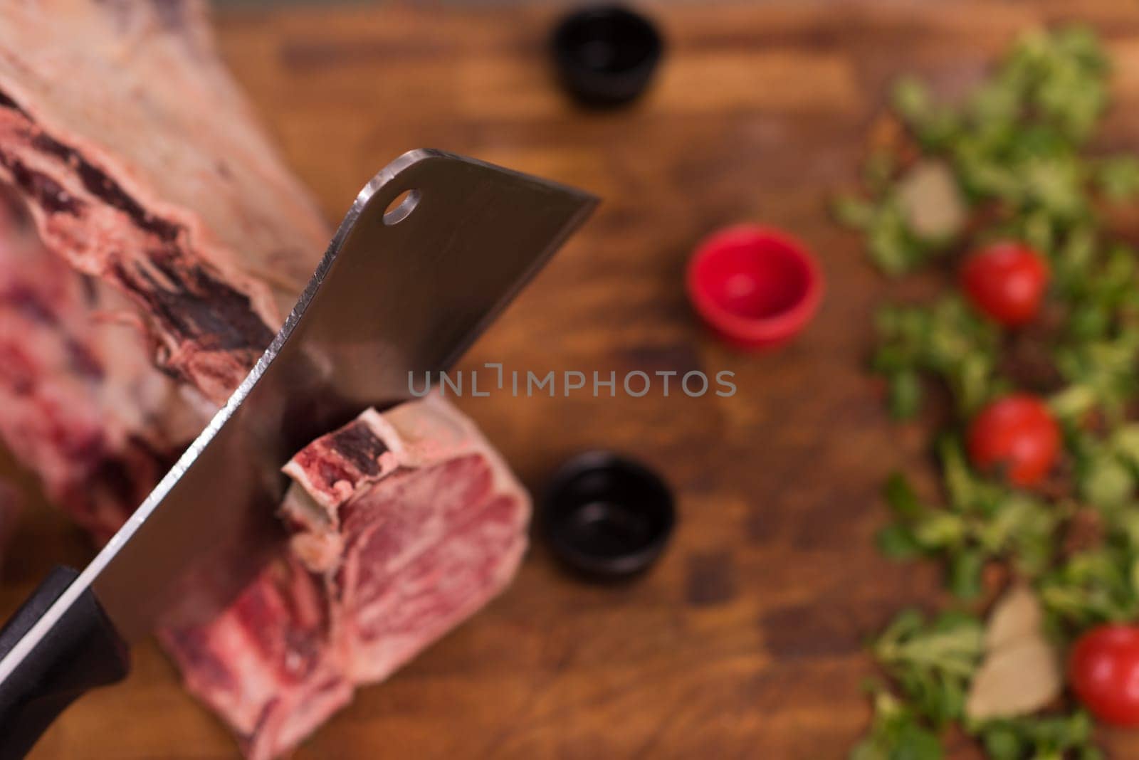 chef using ax while cutting big piece of beef  on wooden board in restaurant kitchen