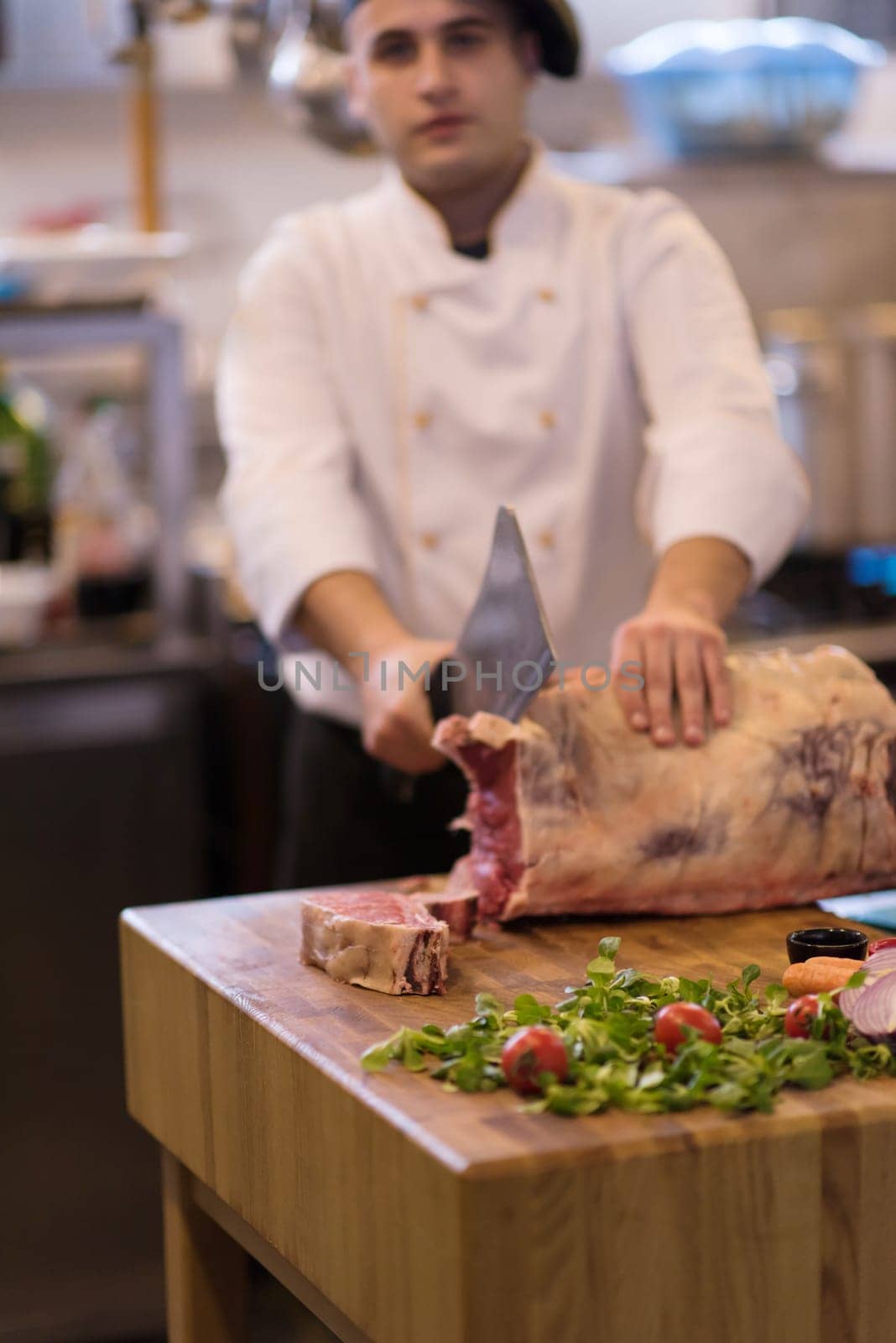 chef using ax while cutting big piece of beef  on wooden board in restaurant kitchen