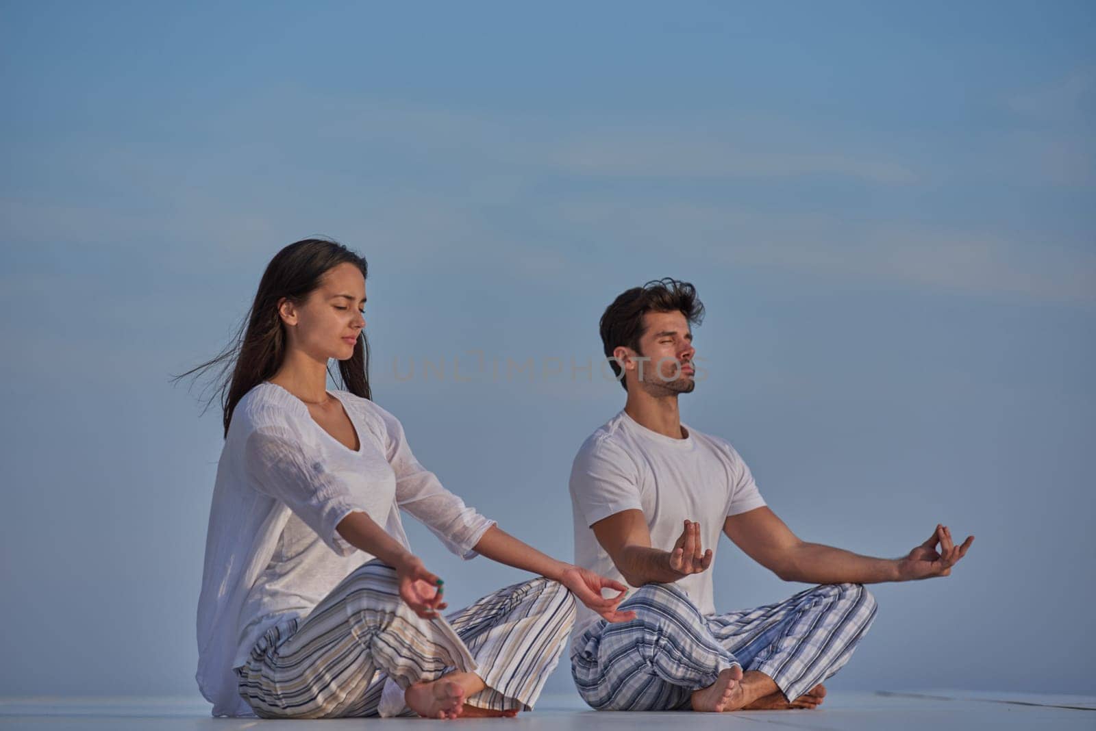 young couple practicing yoga at sunset in modern home terace with ocean and sunset in background