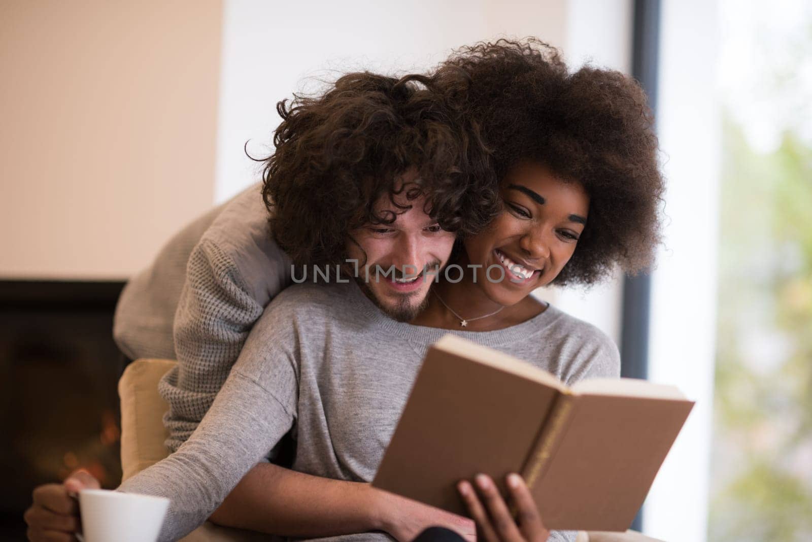 Young beautiful multiethnic couple hugging in front of fireplace at home when reading a book at autumn day