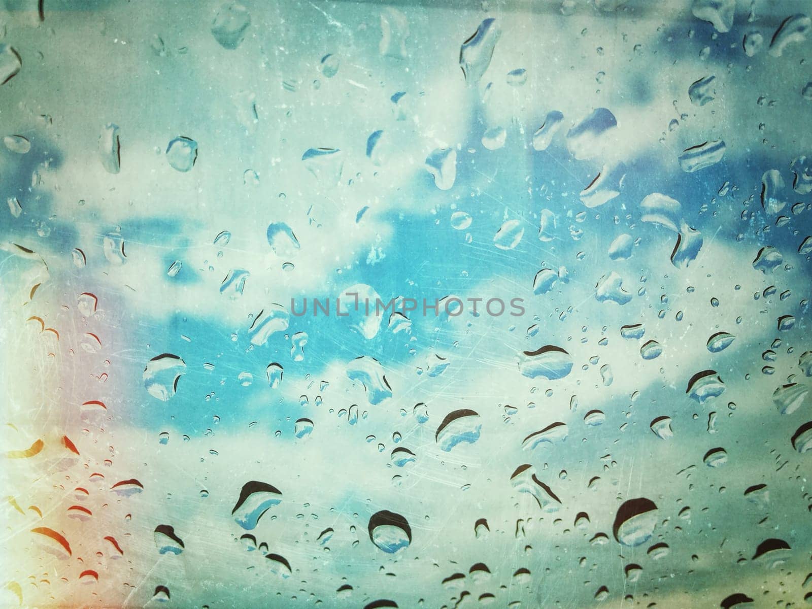 Water drops on window with blue cloudy sky behind