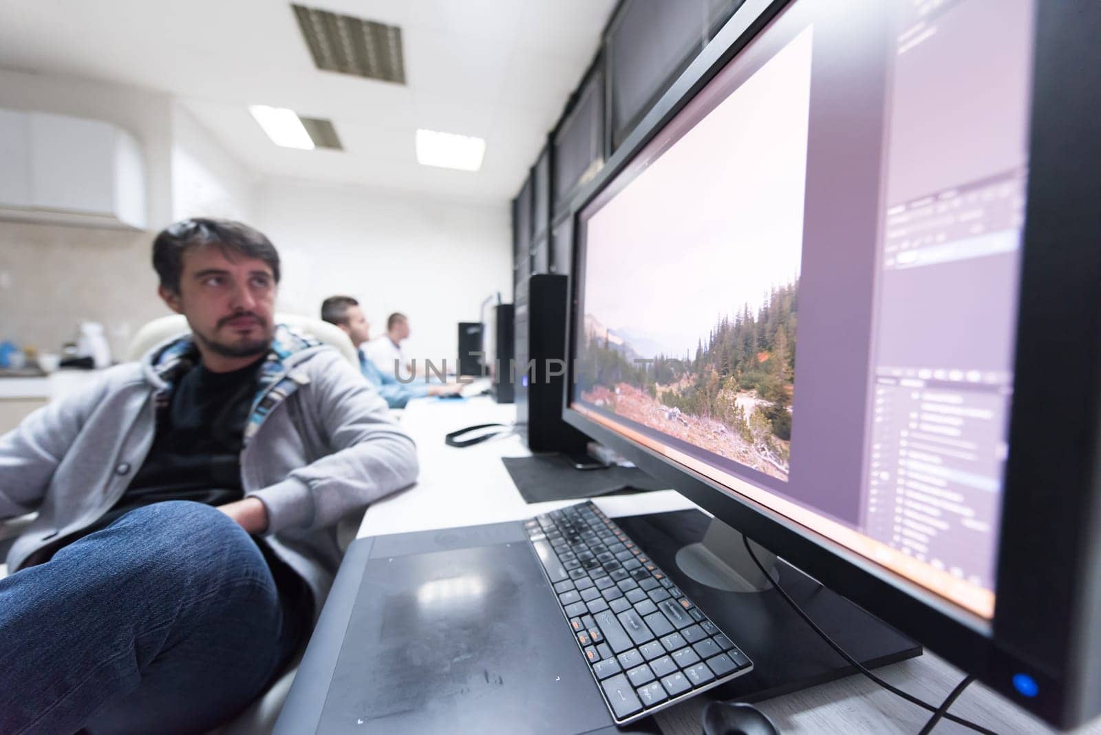 creative worker, photo editor working on graphic tablet at his desktop computer at small startup office