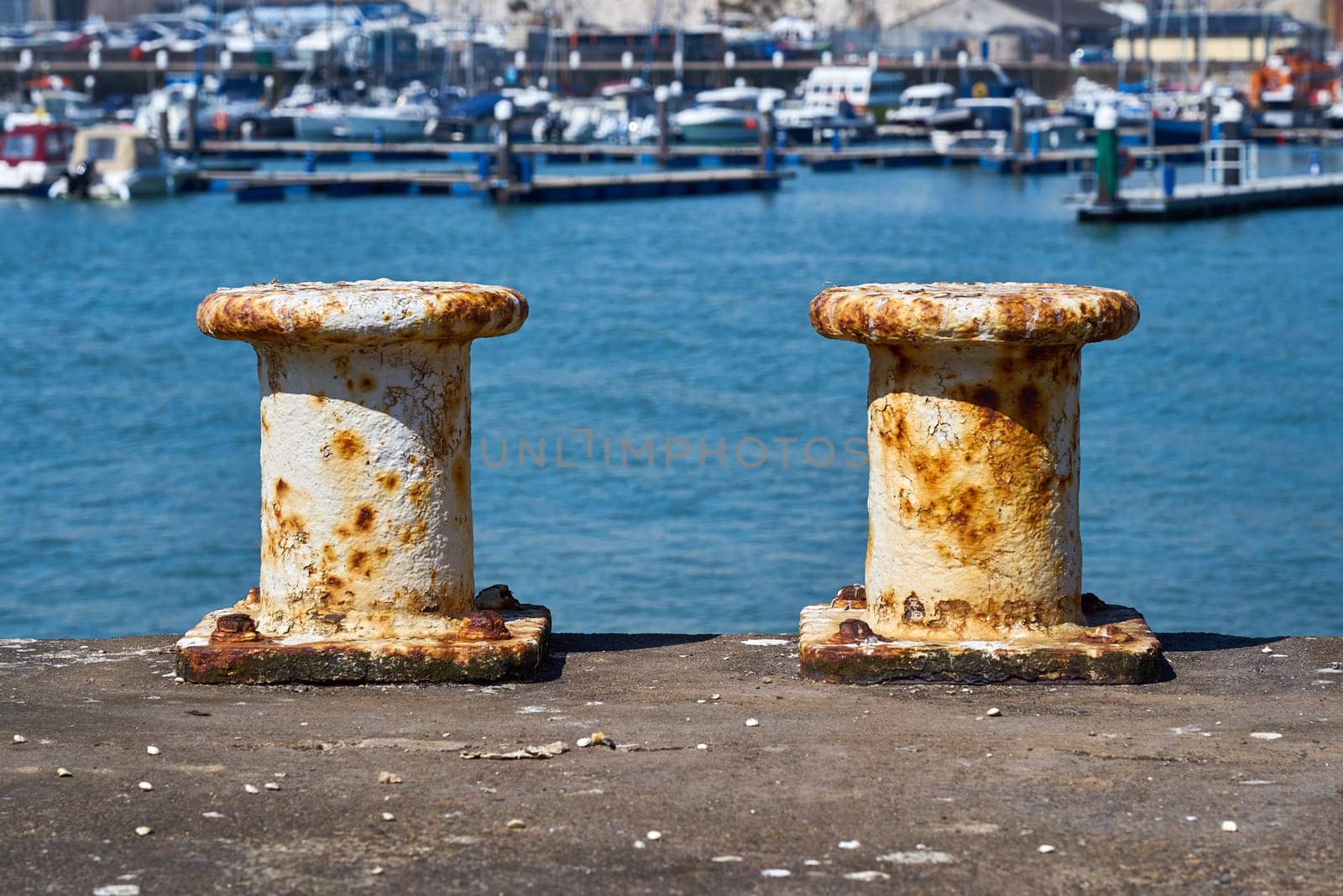 Each white painted steel mooring bollard is showing signs of rust. The pillar bollards are used by ships to moor while in dock.