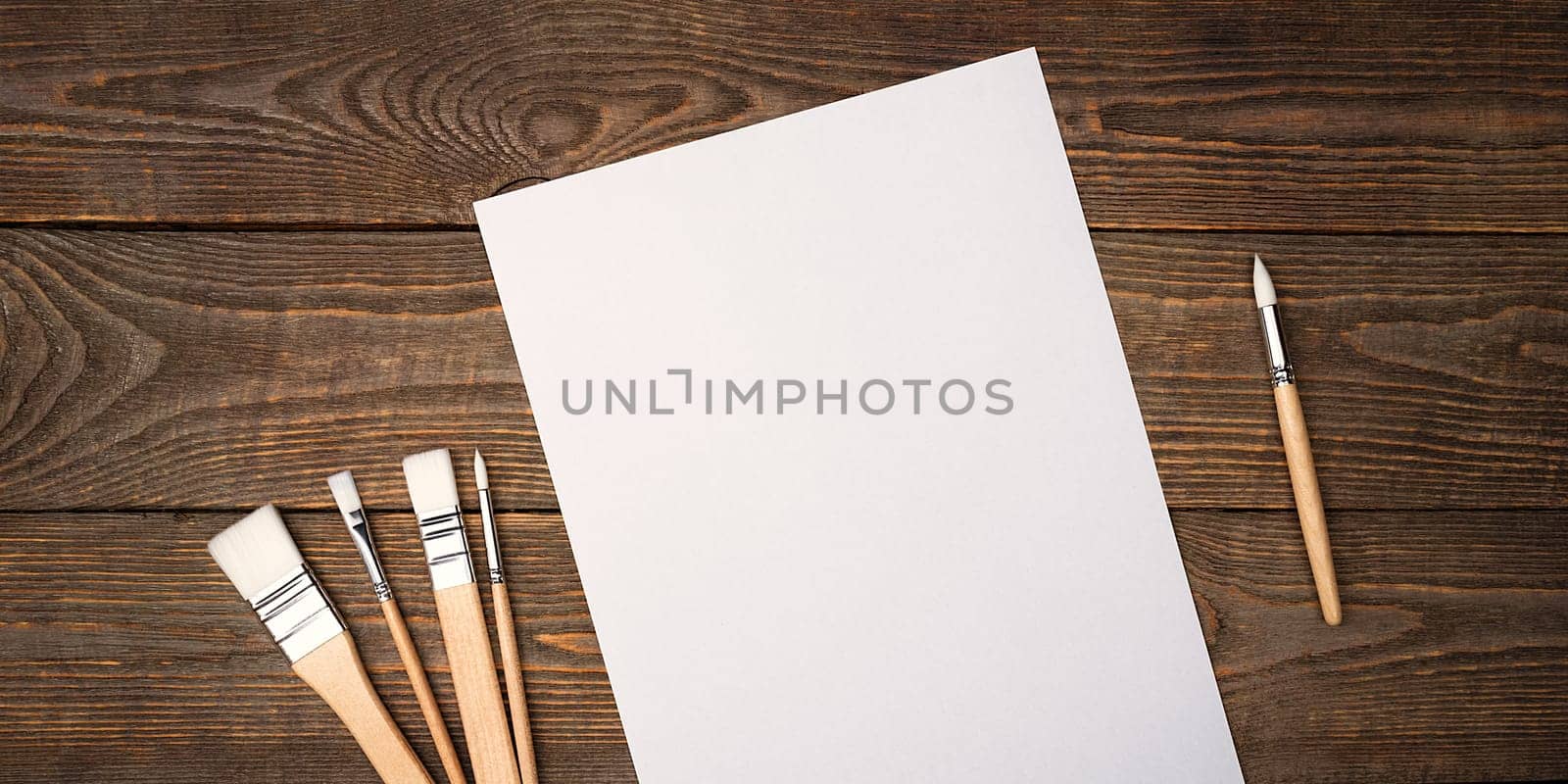 A clean white sheet and brushes on a textured background with space to copy. Layout, mockup space for text and drawing.