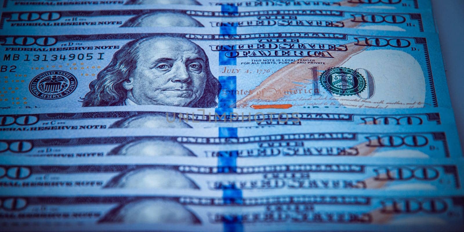 One hundred dollar bills are in a row, one stands out, selective focus. Style blue color.