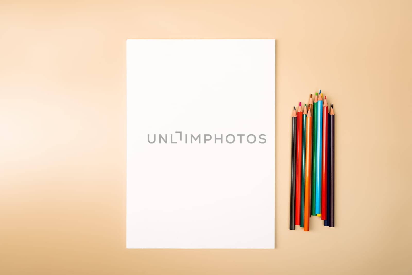 A blank white sheet and colored pencils for drawing on a plain textured background with space for copying and lettering. Layout, mockup free space.