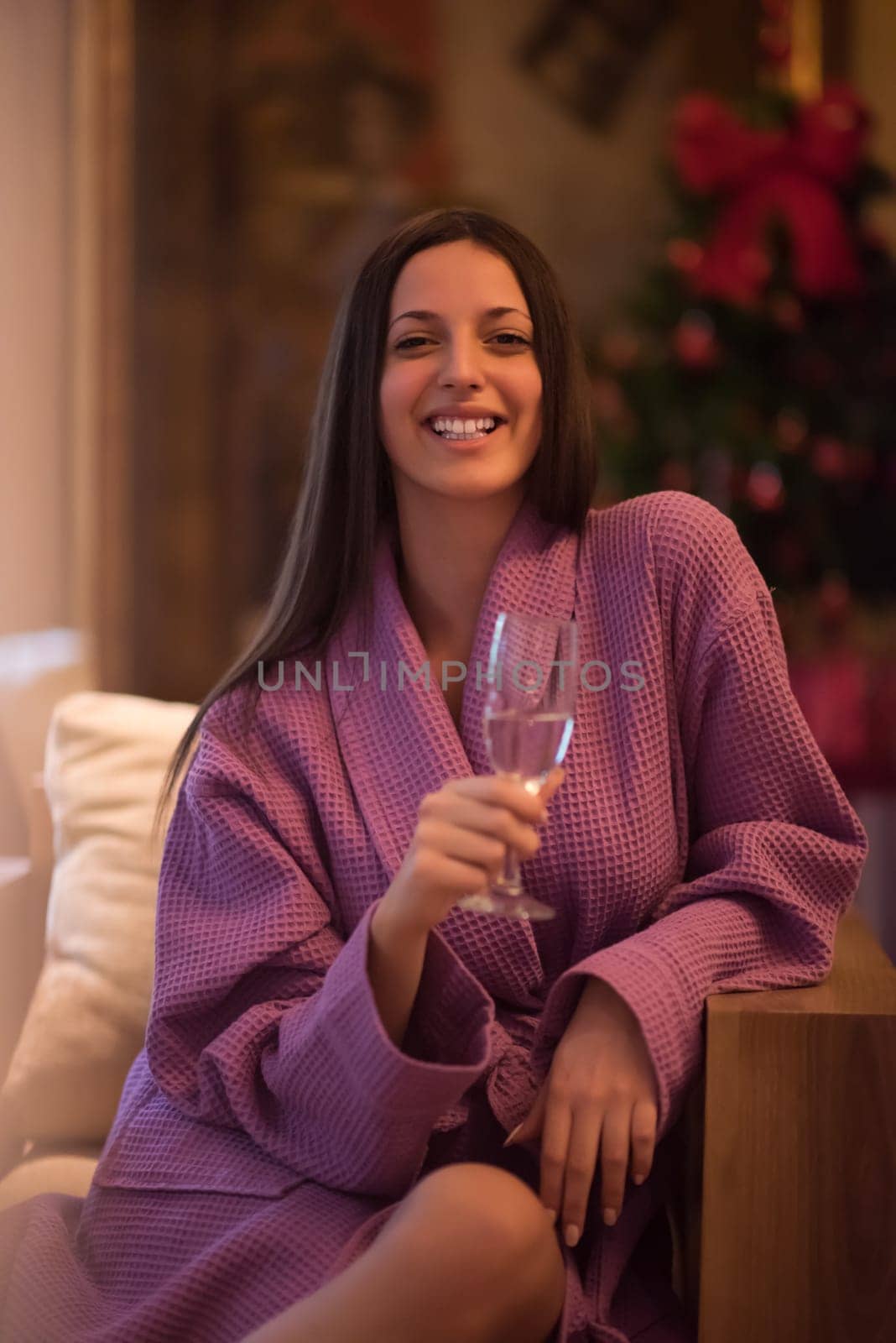 people, and relaxation concept   beautiful young woman in bath robe drinking champagne at spa over holidays lights background