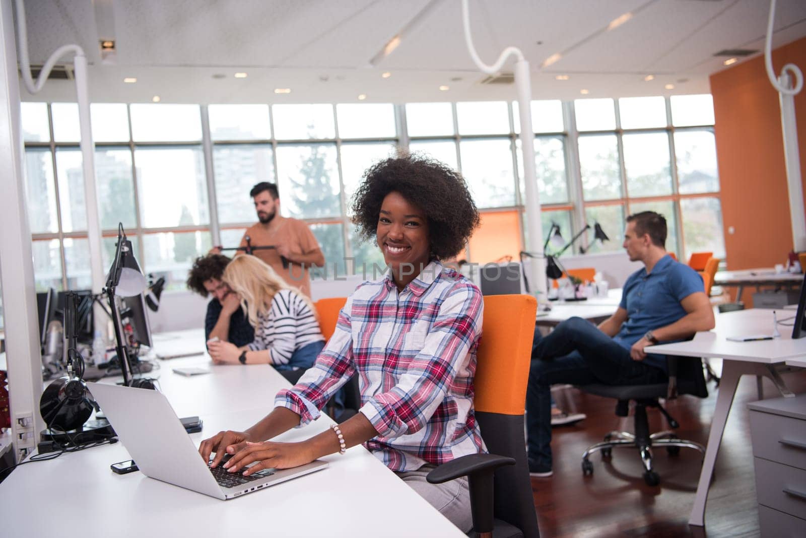young smiling African American informal businesswoman working in the office with colleagues in the background