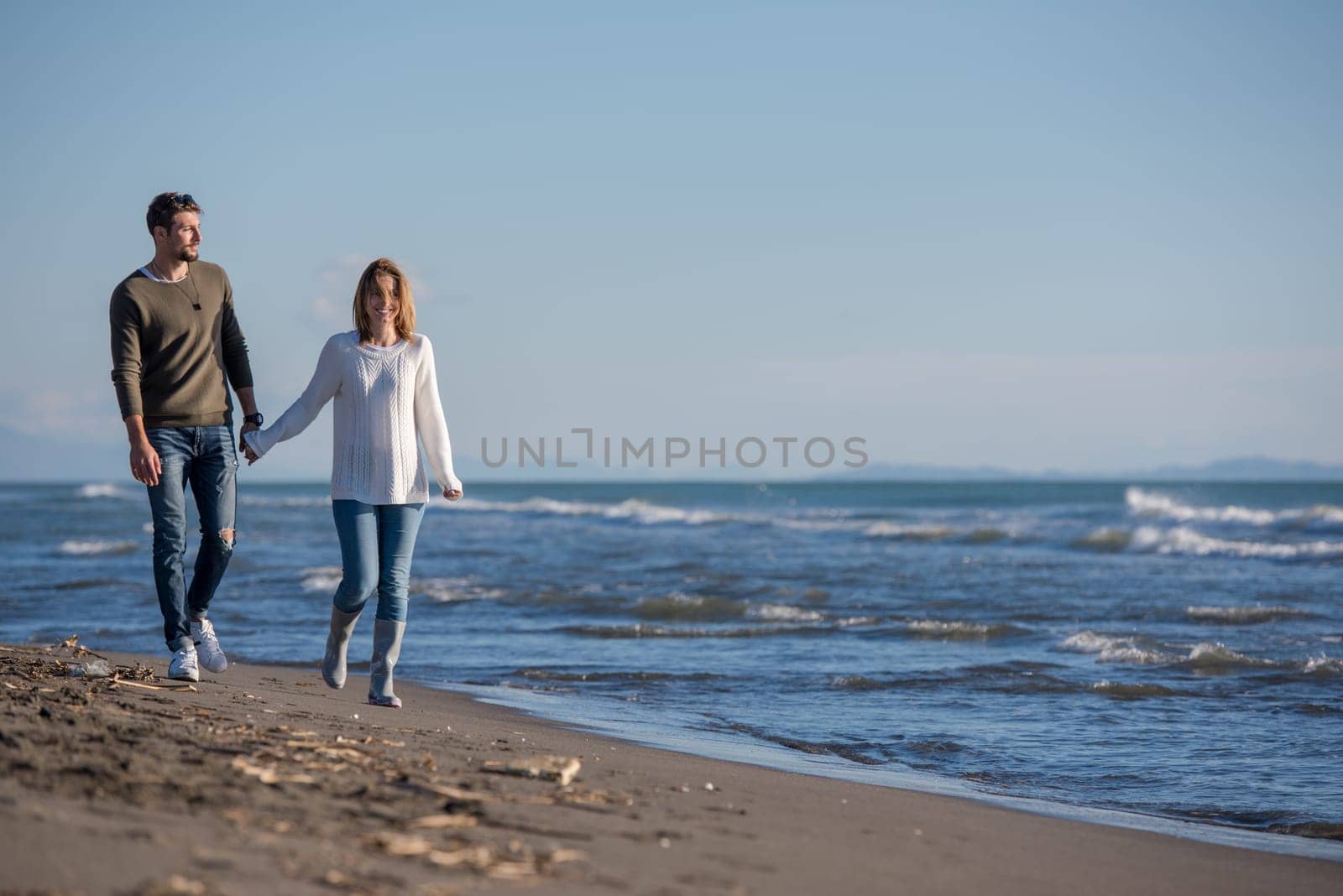 Young couple having fun walking and hugging on beach during autumn sunny day