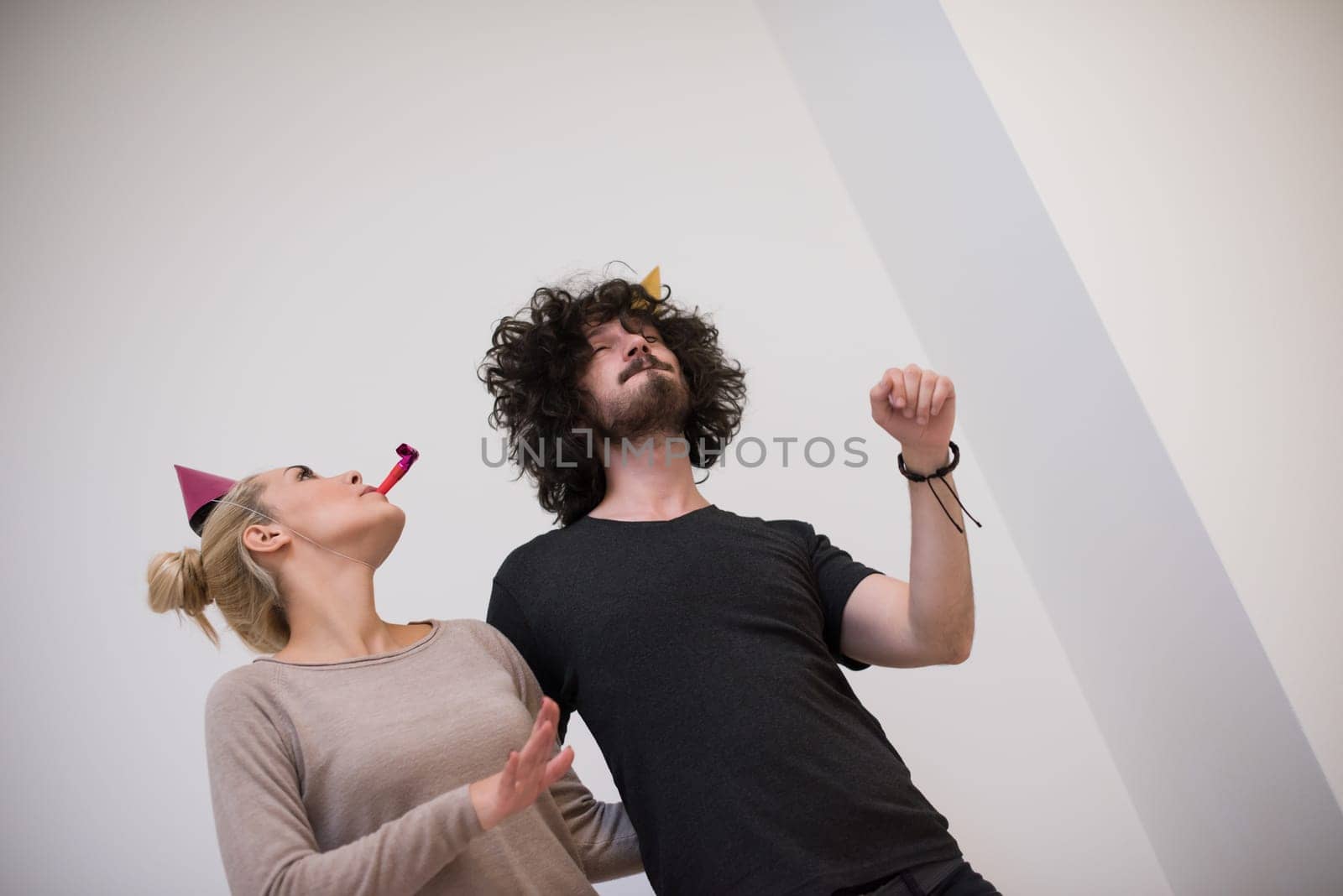 Young happy couple in party hats blowing in whistle isolated on a white background