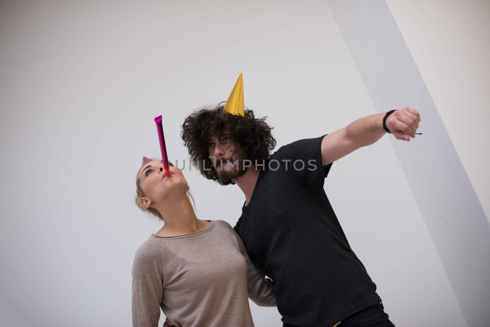 Young happy couple in party hats blowing in whistle isolated on a white background