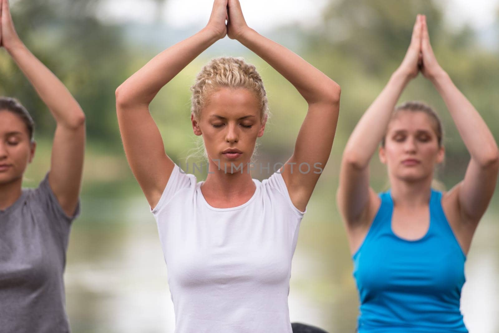 group of young healthy women relaxing while meditating and doing yoga exercise in the beautiful nature on the bank of the river