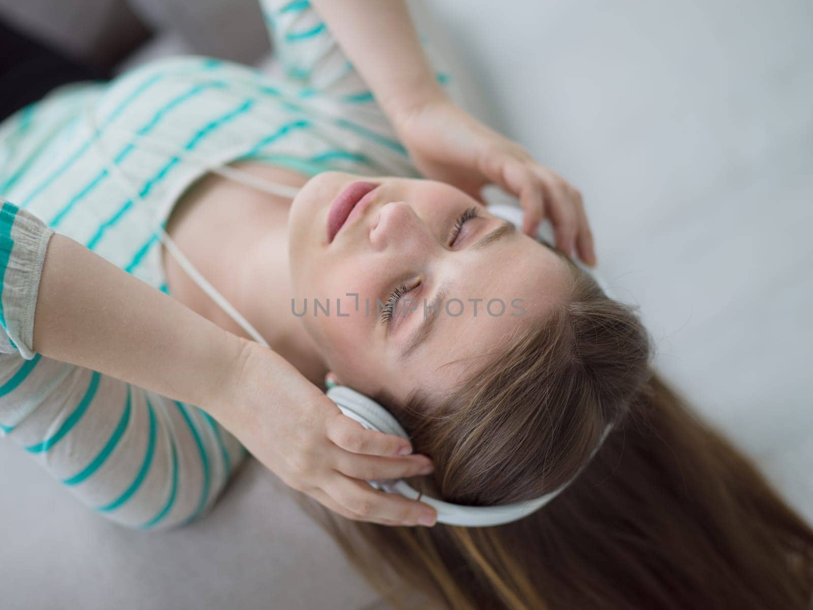 Young beautiful girl enjoying music through headphones, laying on sofa at home