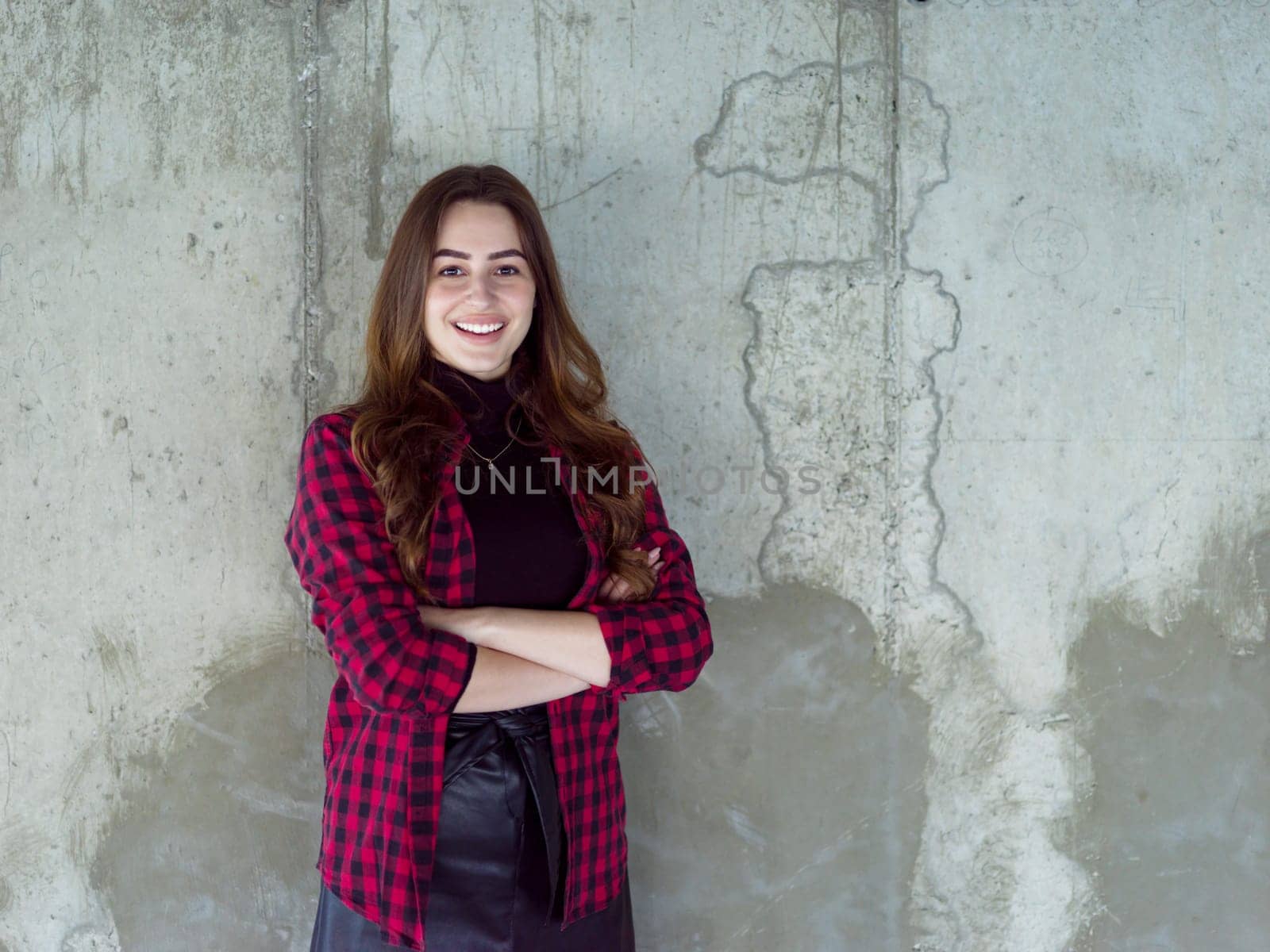 portrait of young successful smiling casual businesswoman standing in front of a concrete wall at new startup office