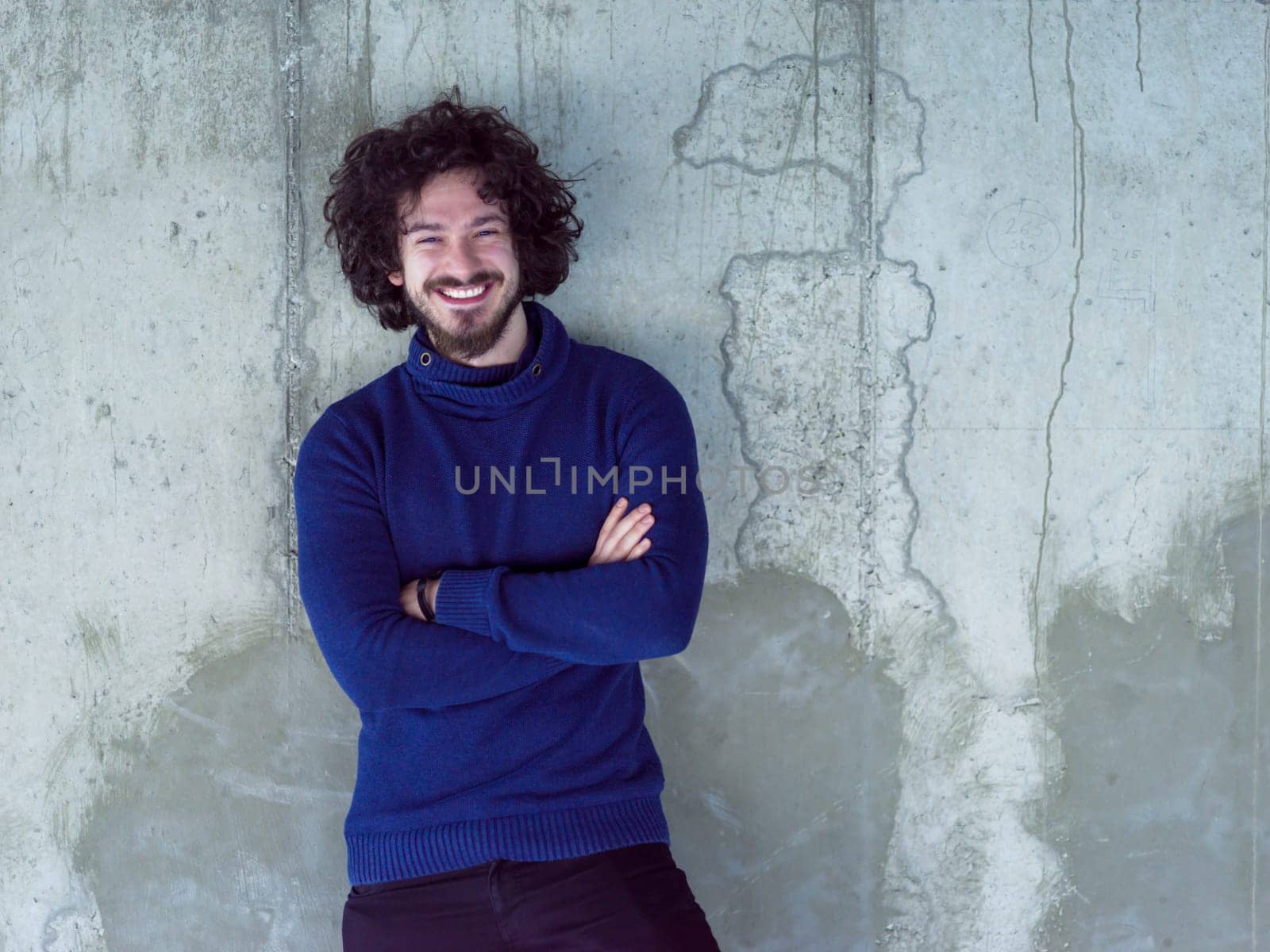 portrait of young successful smiling casual businessman standing in front of a concrete wall at new startup office