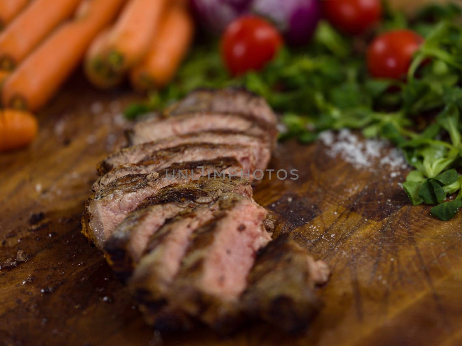Juicy slices of grilled steak  with vegetables around on a wooden board