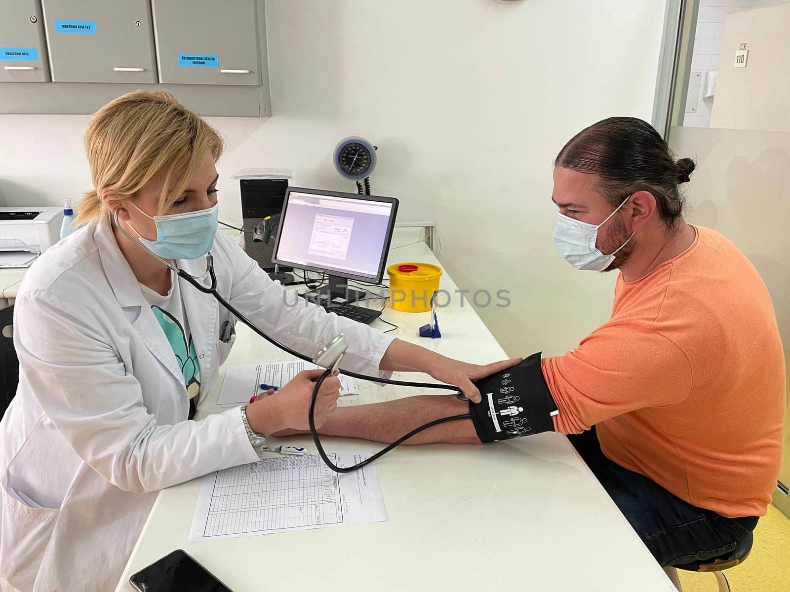 Female doctor in medical facemask measure blood pressure with electronic monitor in hospital. Caring woman GP help examine do checkup of elderly client in clinic. Healthcare, hypertension concept. High quality photo