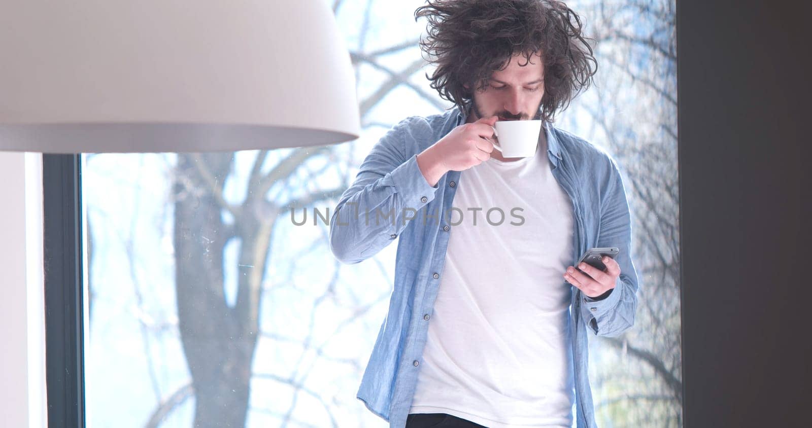 Handsome casual young man drinking coffee and using a mobile phone at  home