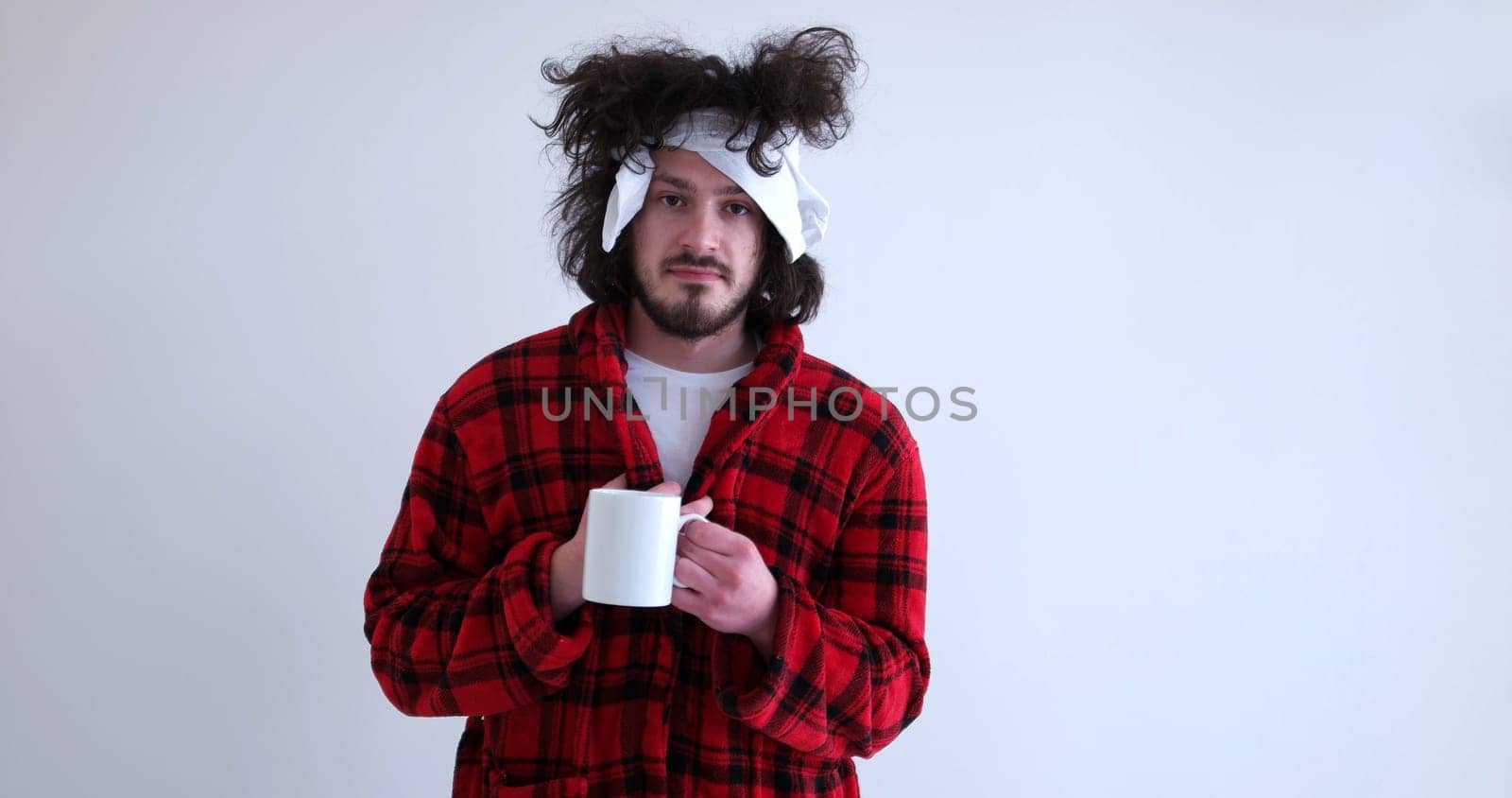 young Man with flu and fever wrapped holding cup of healing tea isolated over white