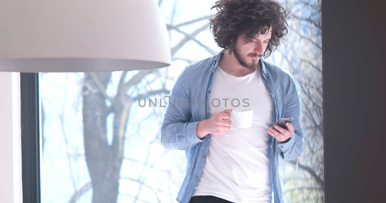 Handsome casual young man drinking coffee and using a mobile phone at  home