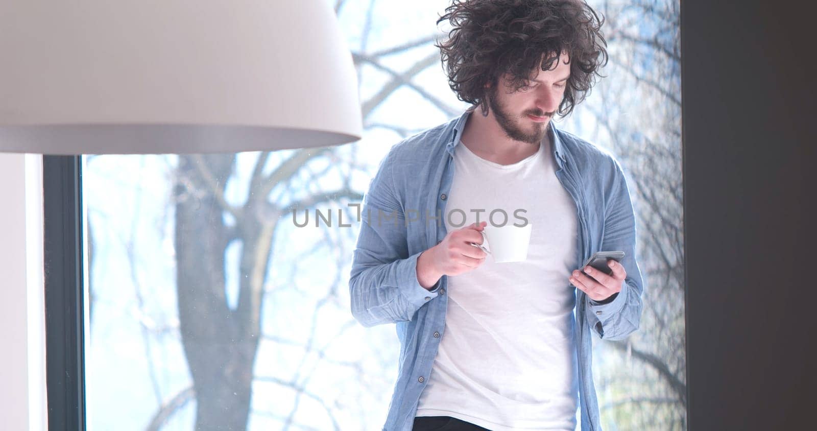 Handsome casual young man drinking coffee and using a mobile phone at  home