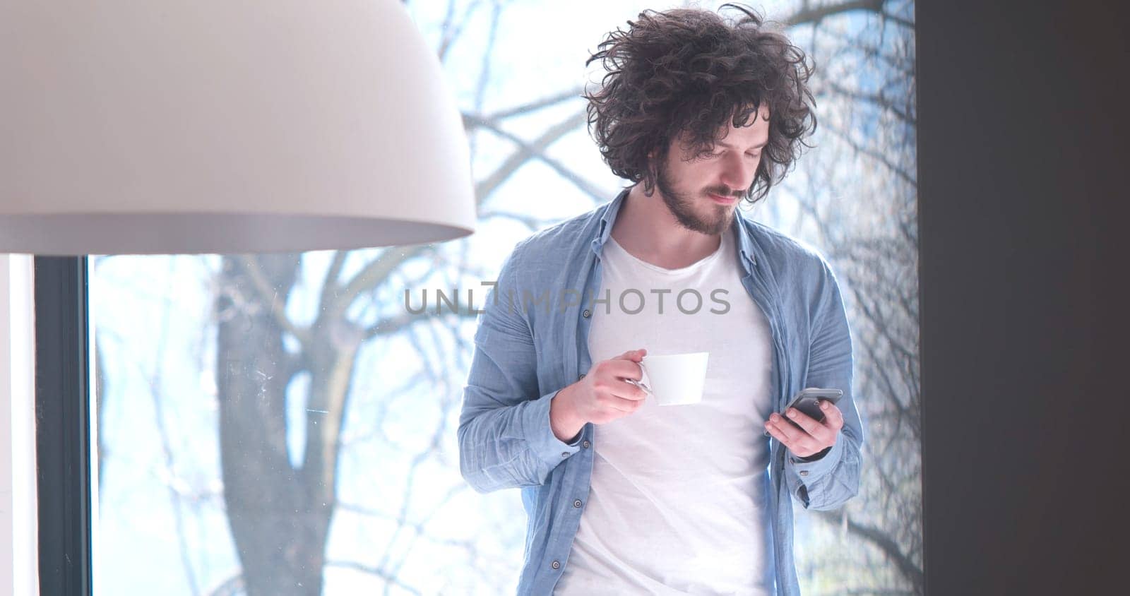 Handsome casual young man drinking coffee and using a mobile phone at  home