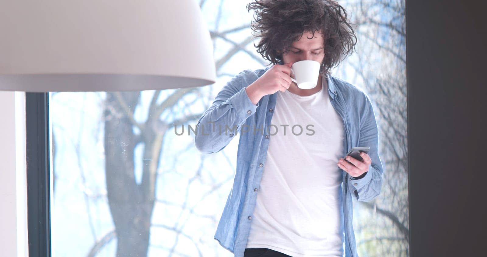 Handsome casual young man drinking coffee and using a mobile phone at  home